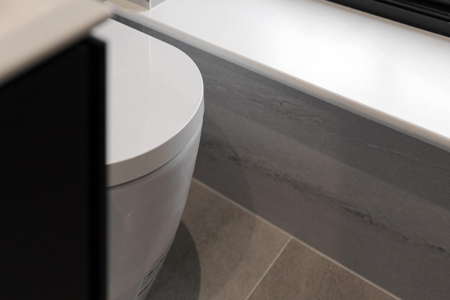 Edge of white toilet surrounded by grey walls and white windowsill
