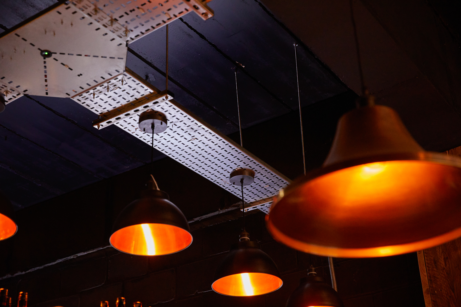 Black ceiling with multiple circular copper pendant lamps hanging