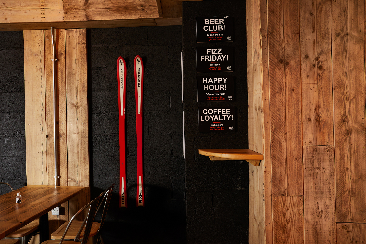 Wooden and black painted brick wall with a pair of red skis hung up and cafe promotional posters