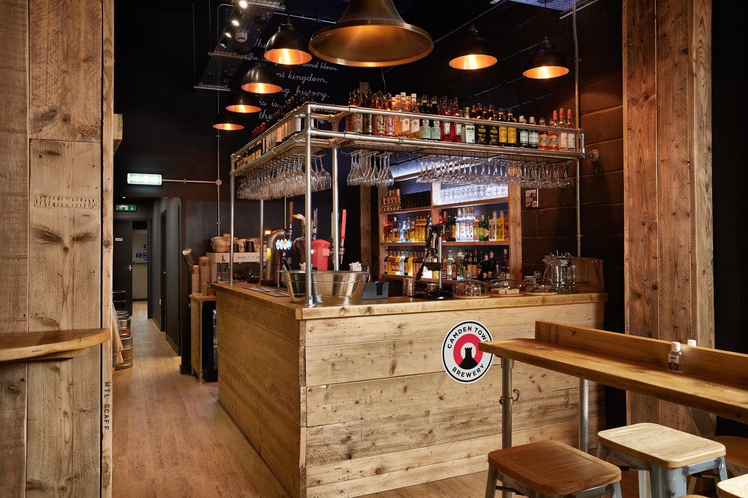 Wooden bar area with bottles on metal shelving and circular pendant lights hanging above
