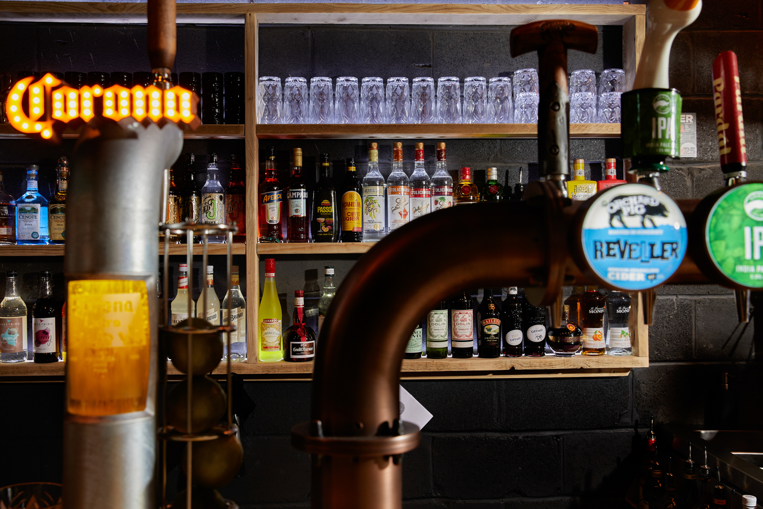 Bar area with wooden shelves along black painted brick wall holding glasses and bottles