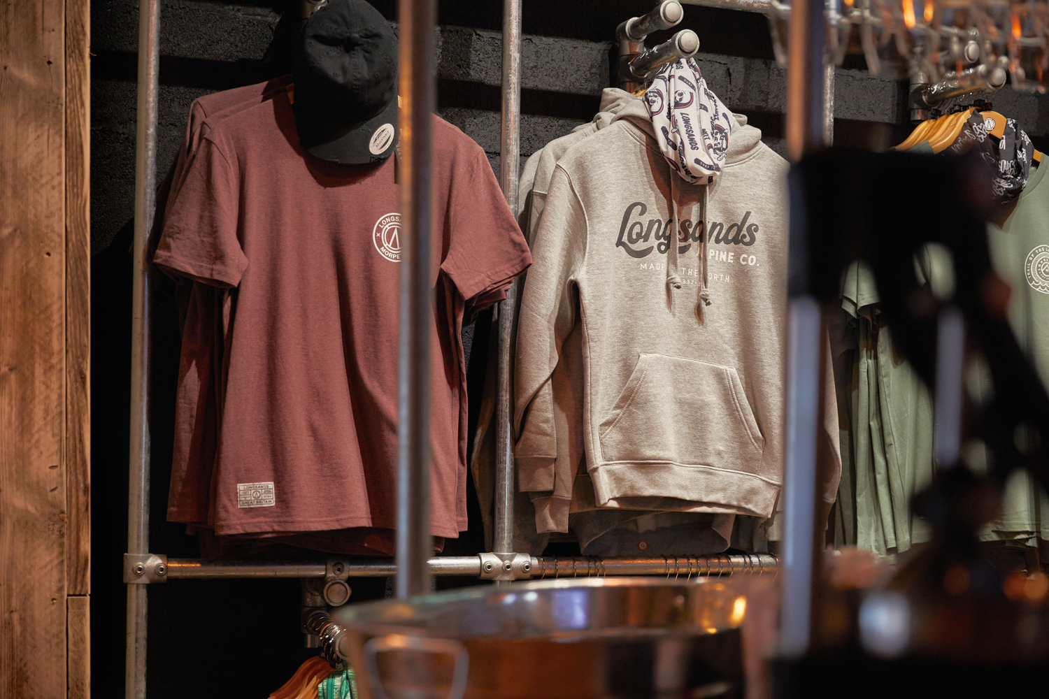 T-shirts and hoodies hung up from metal clothes rails against black painted brick wall
