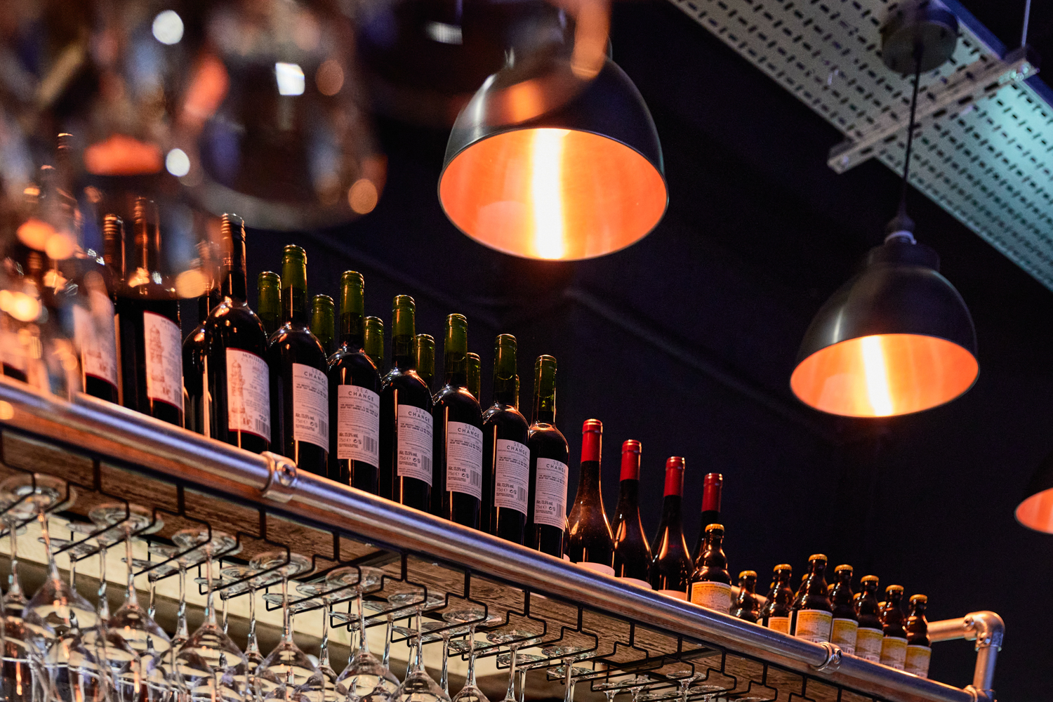Close up on shelving above bar holding bottles and glasses hanging from the underside