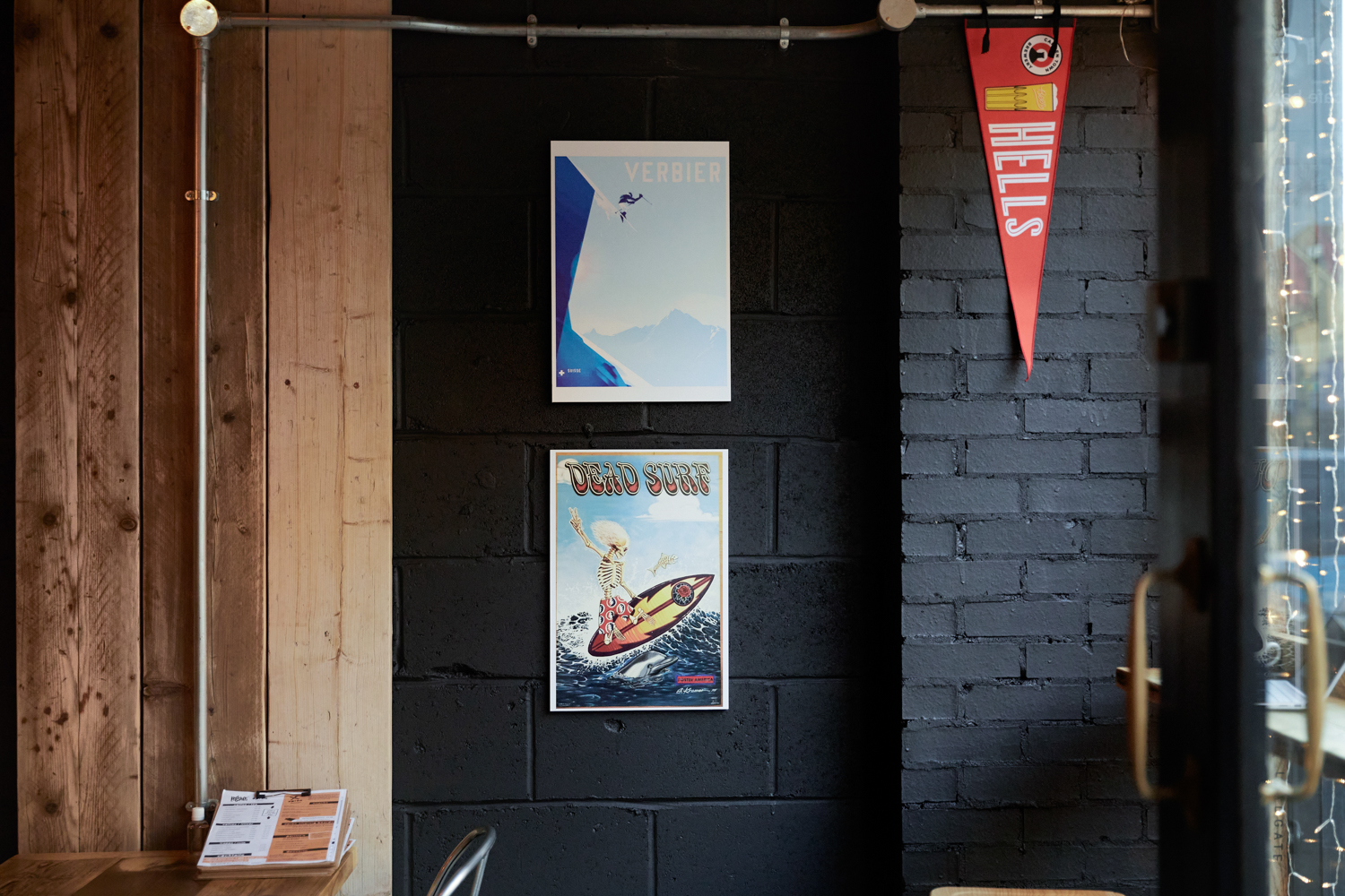 Black painted brick wall featuring two ski-inspired posters with wooden panelling on the wall to the left