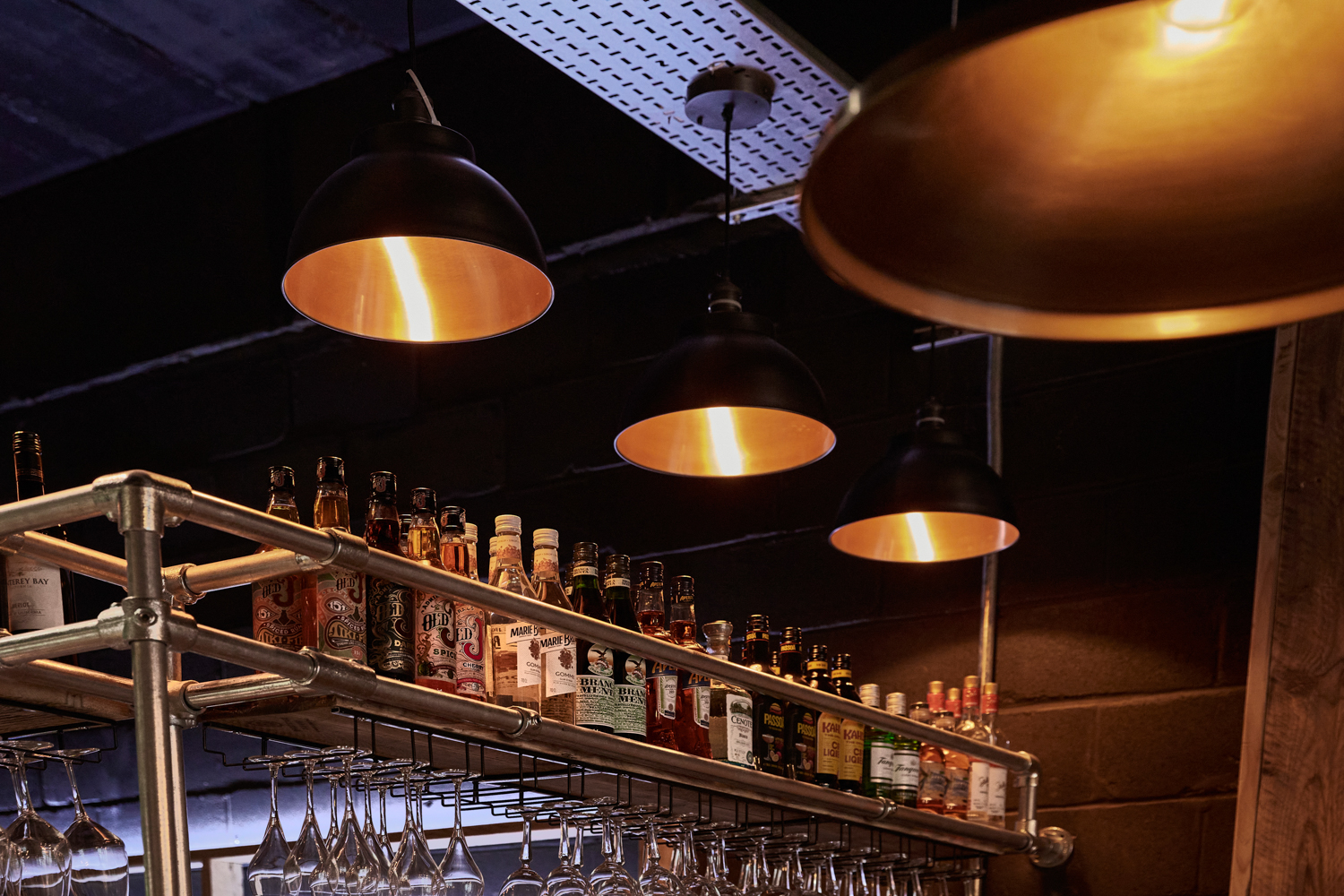 Shelving above bar area holding bottles with circular pendant lights hanging from the ceiling above