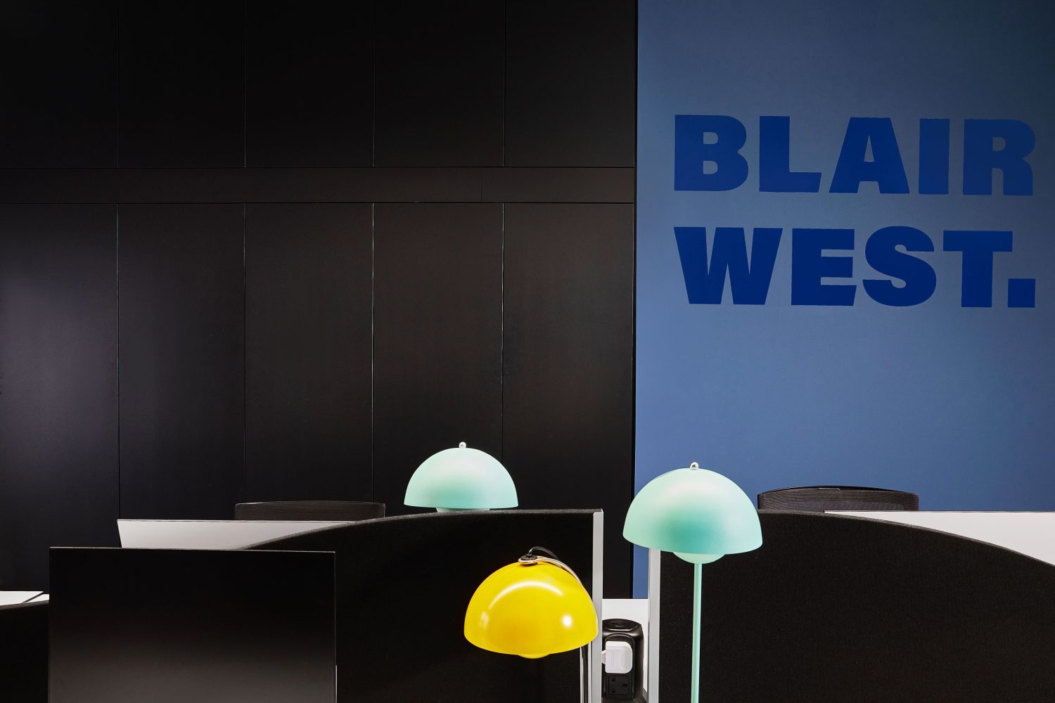Office desks with yellow and blue table lamps and large blue graphic on wall behind