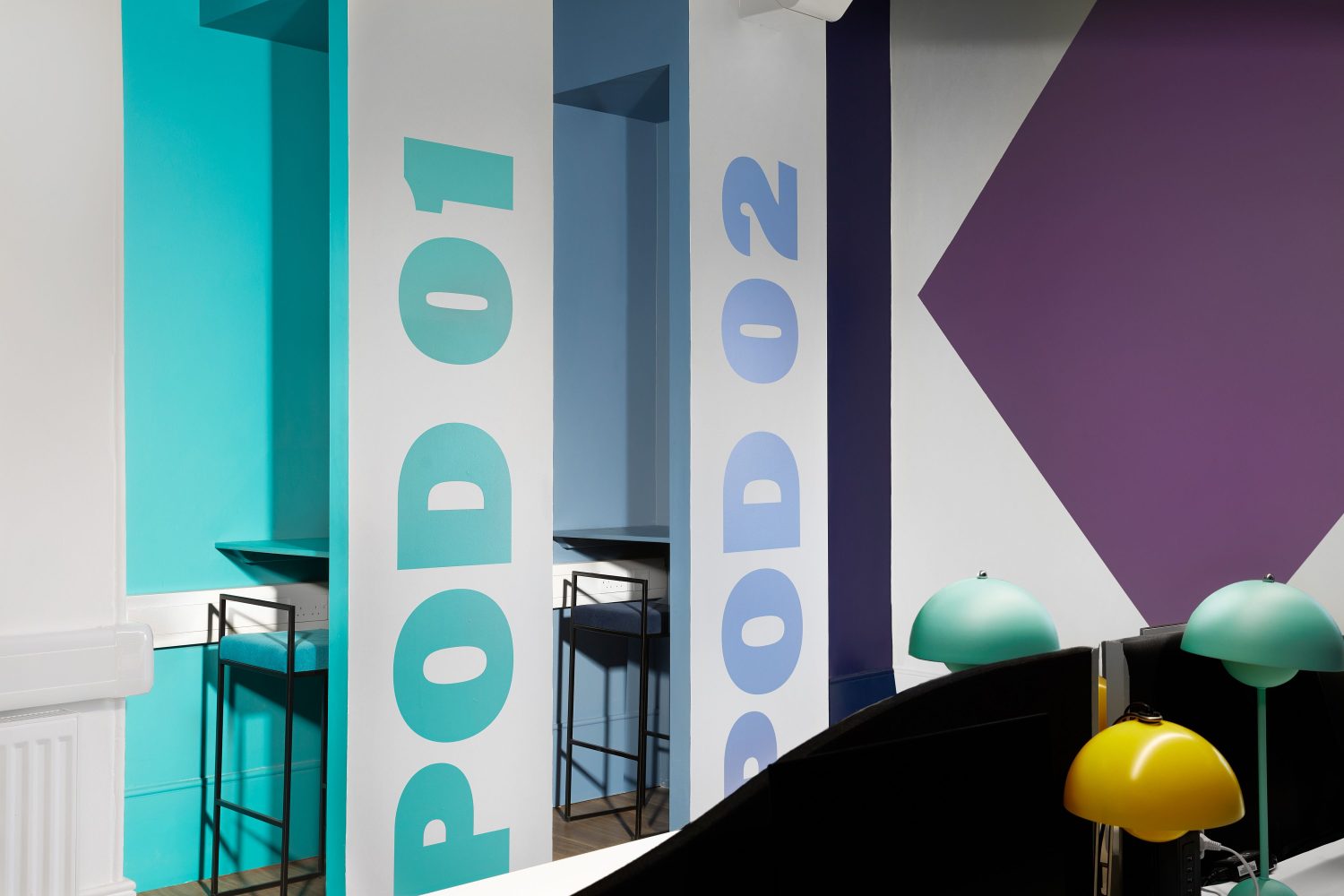 Two work pods with desks for singular people and large blue and purple graphics on the side walls