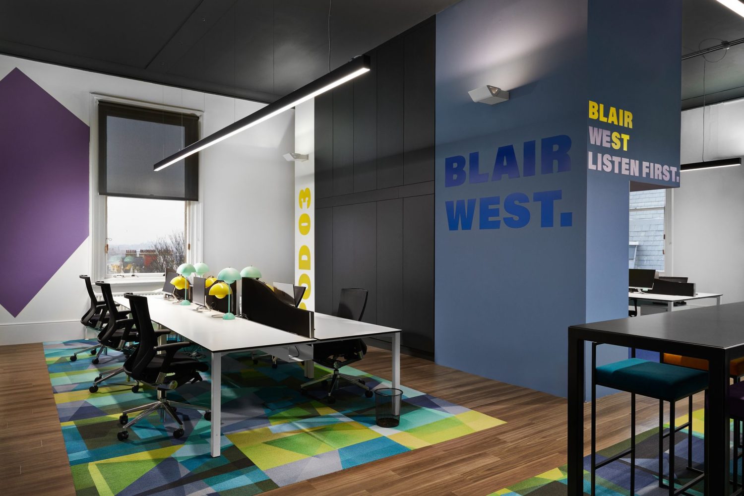 Open plan office desk area with green and blue geometric flooring and blue wall with large text graphics on it