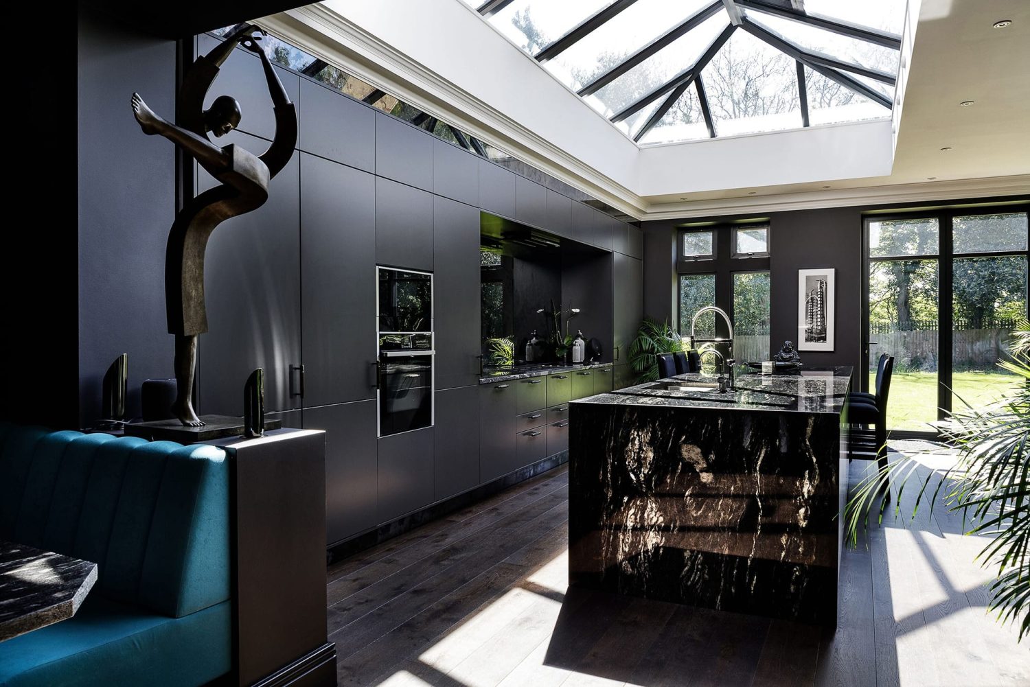 Kitchen with black walls and cabinets to the left with a large dark marble island in the centre and abstract ornament to the left