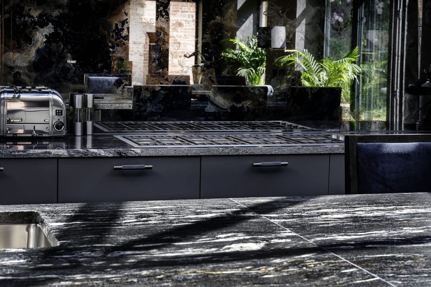 Dark grey marble kitchen countertop with stove area behind with antique mirror backsplash