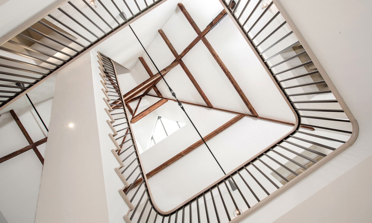 Lookin up from beneath spiral staircase to white ceiling with wooden beams across