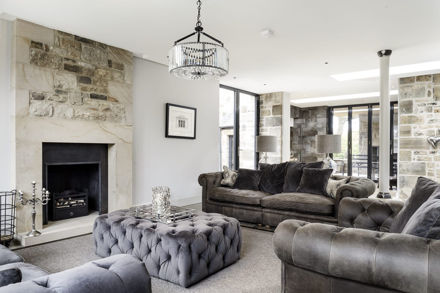 Living room with grey sofas and exposed stone around fireplace and circular glass pendant light from ceiling