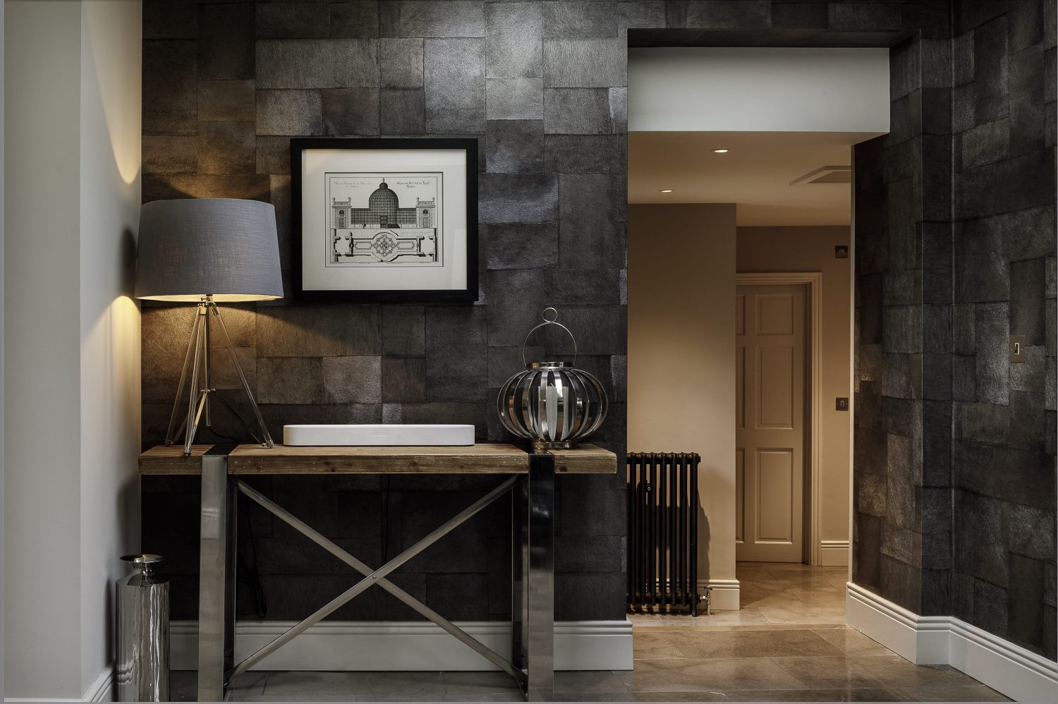 Hallway with dark grey tiled walls and wooden table with chrome legs and framed artwork above