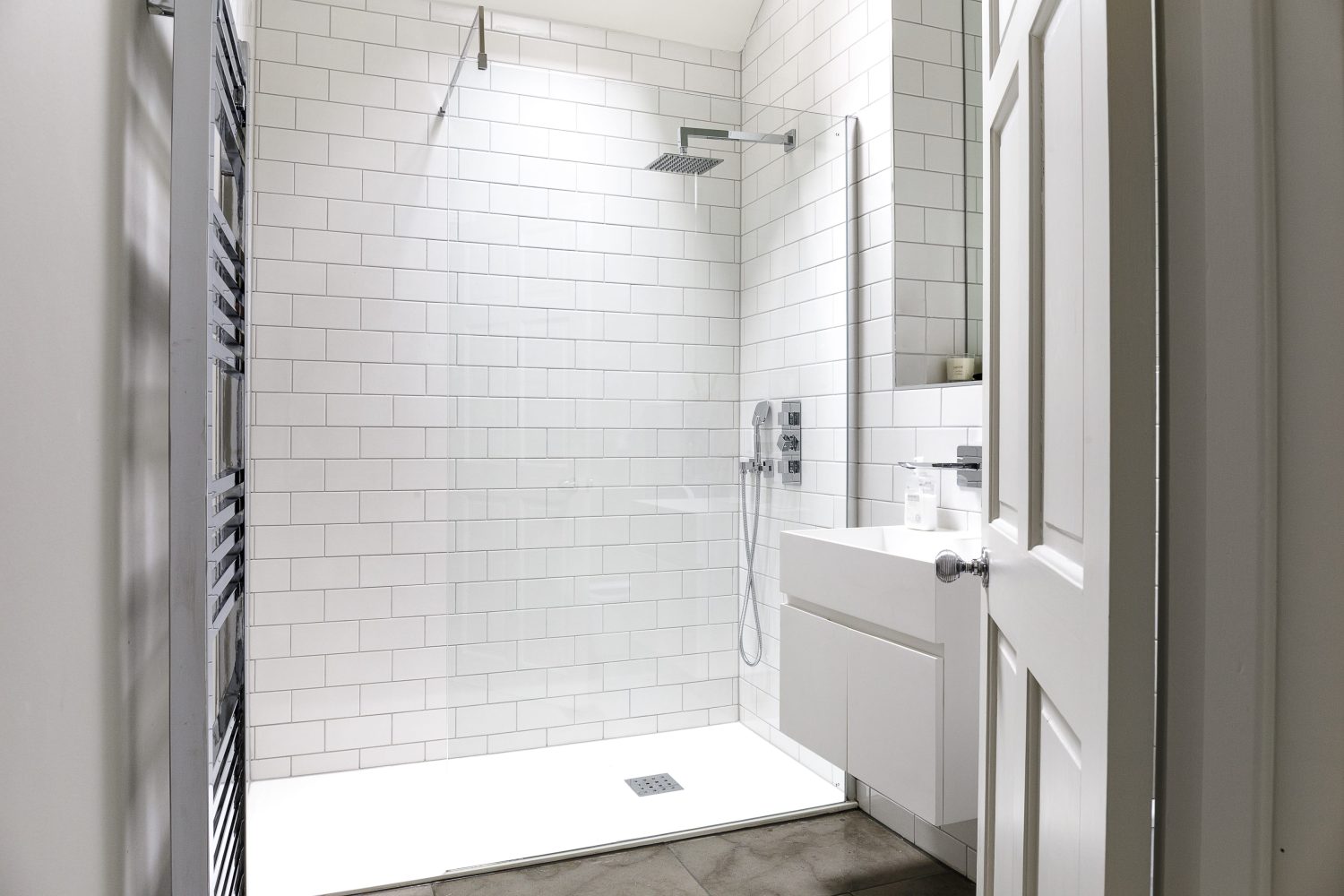 Bathroom with white tiled walls and white sink next to shower with glass door