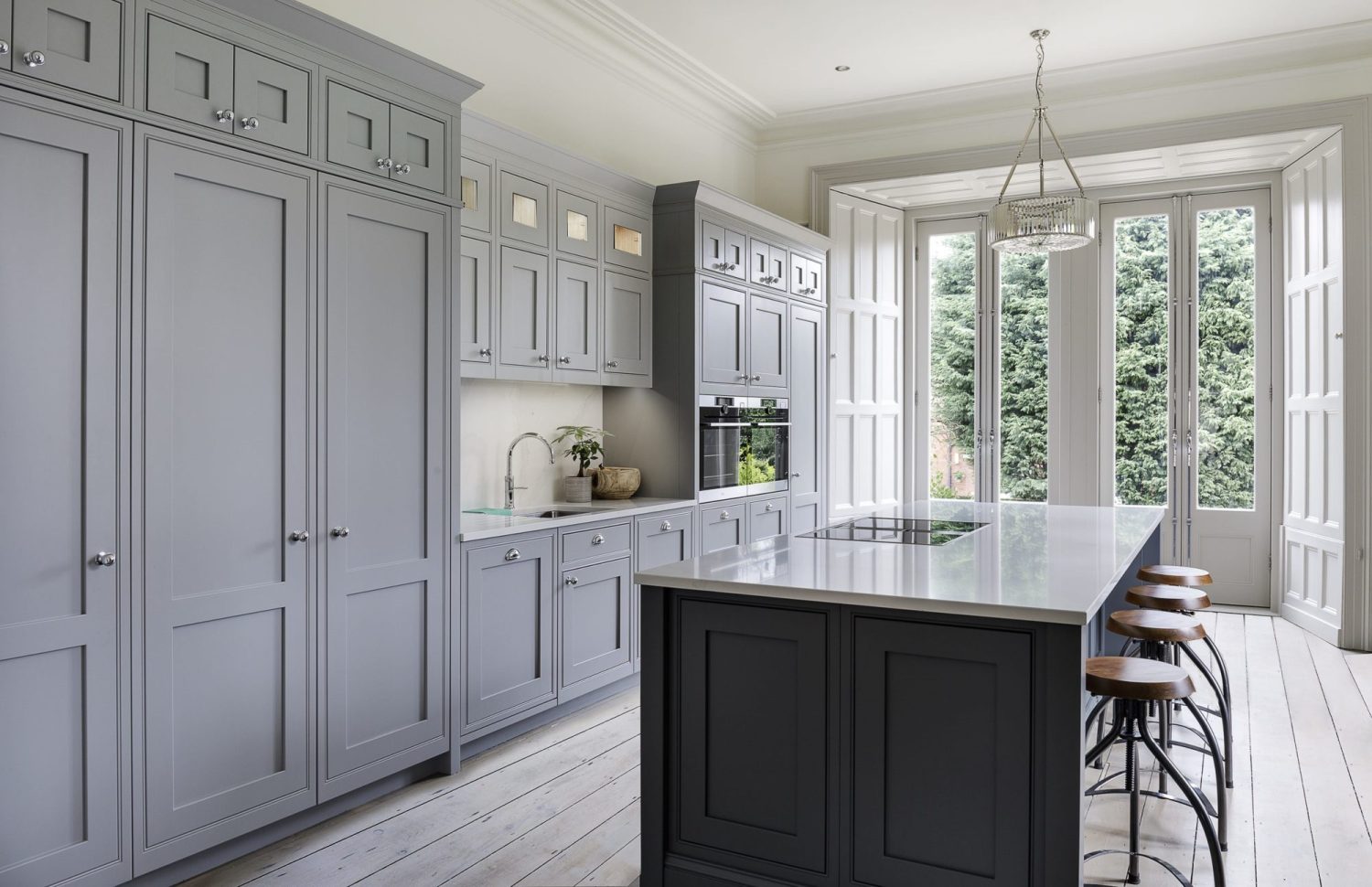 Kitchen with grey cabinets along wall and island in the centre with white countertops and double french doors leading outside