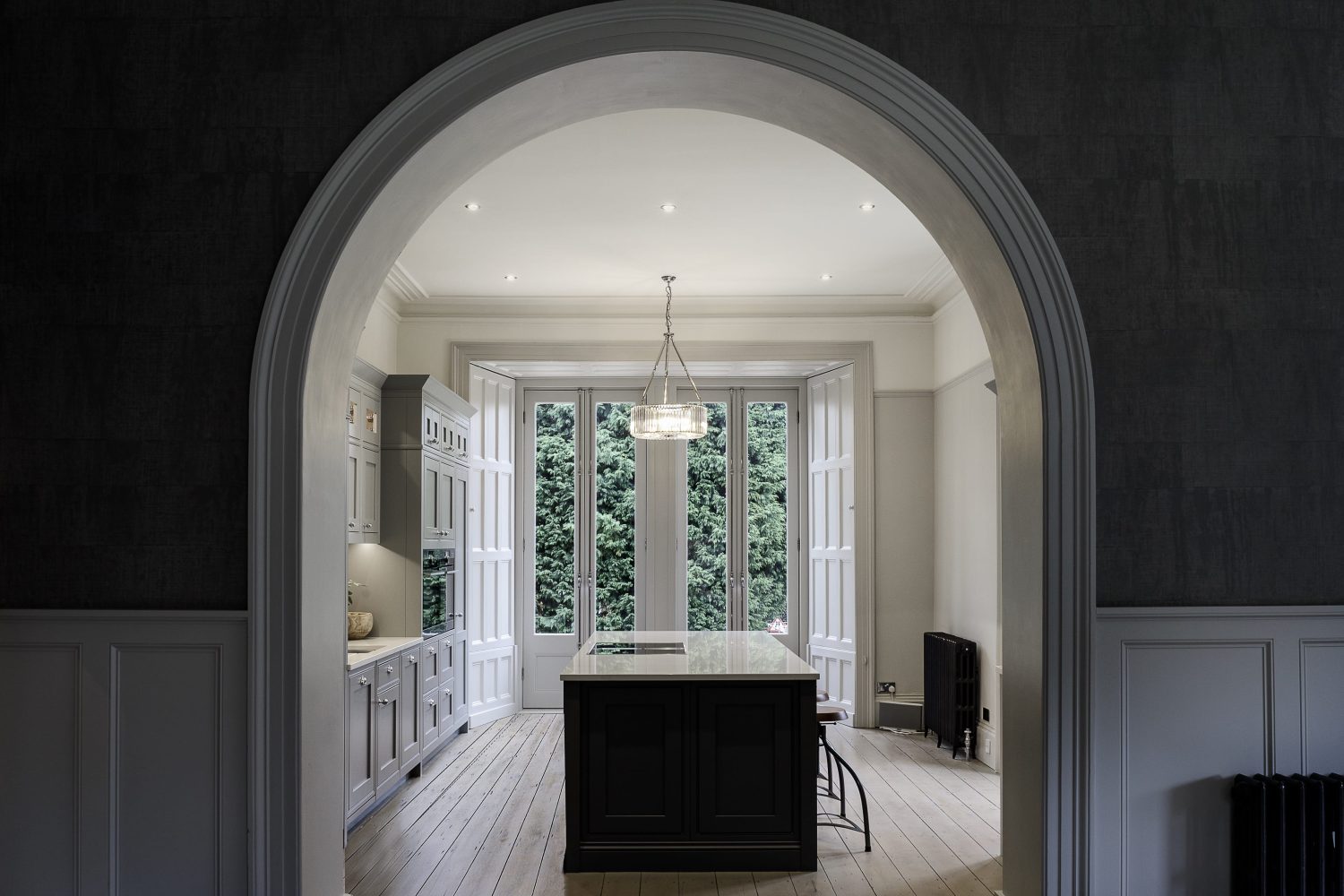 White archway surrounded by grey walls looking through to kitchen with white double french doors leading outside