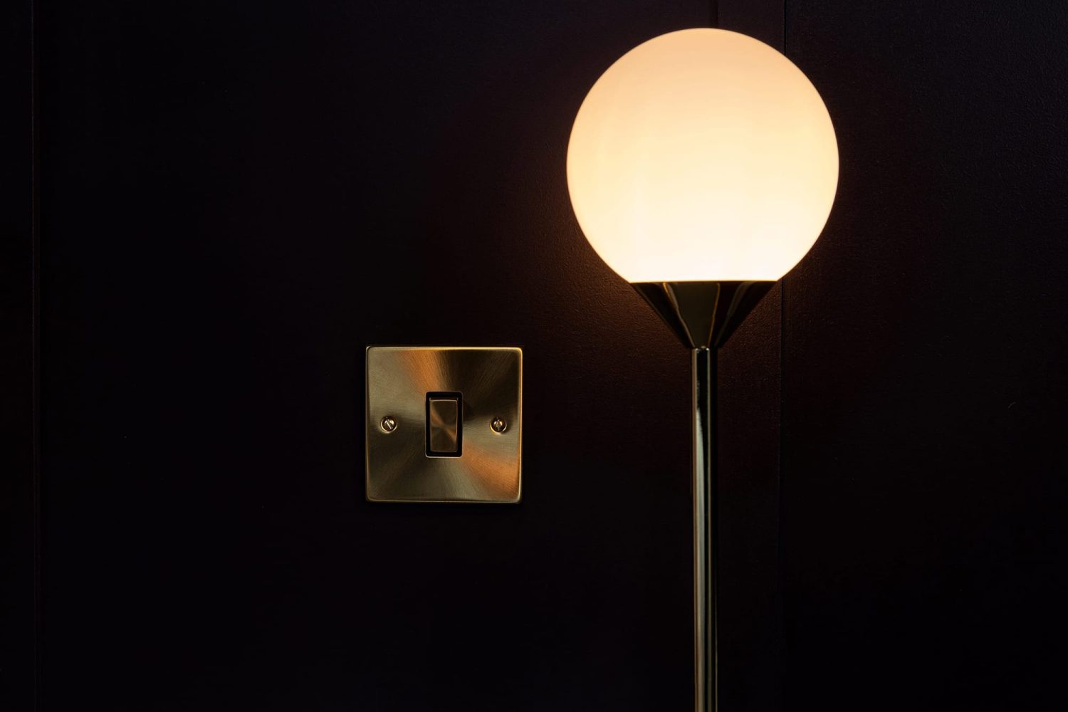 Circular glowing light on dark wall beside gold light switch