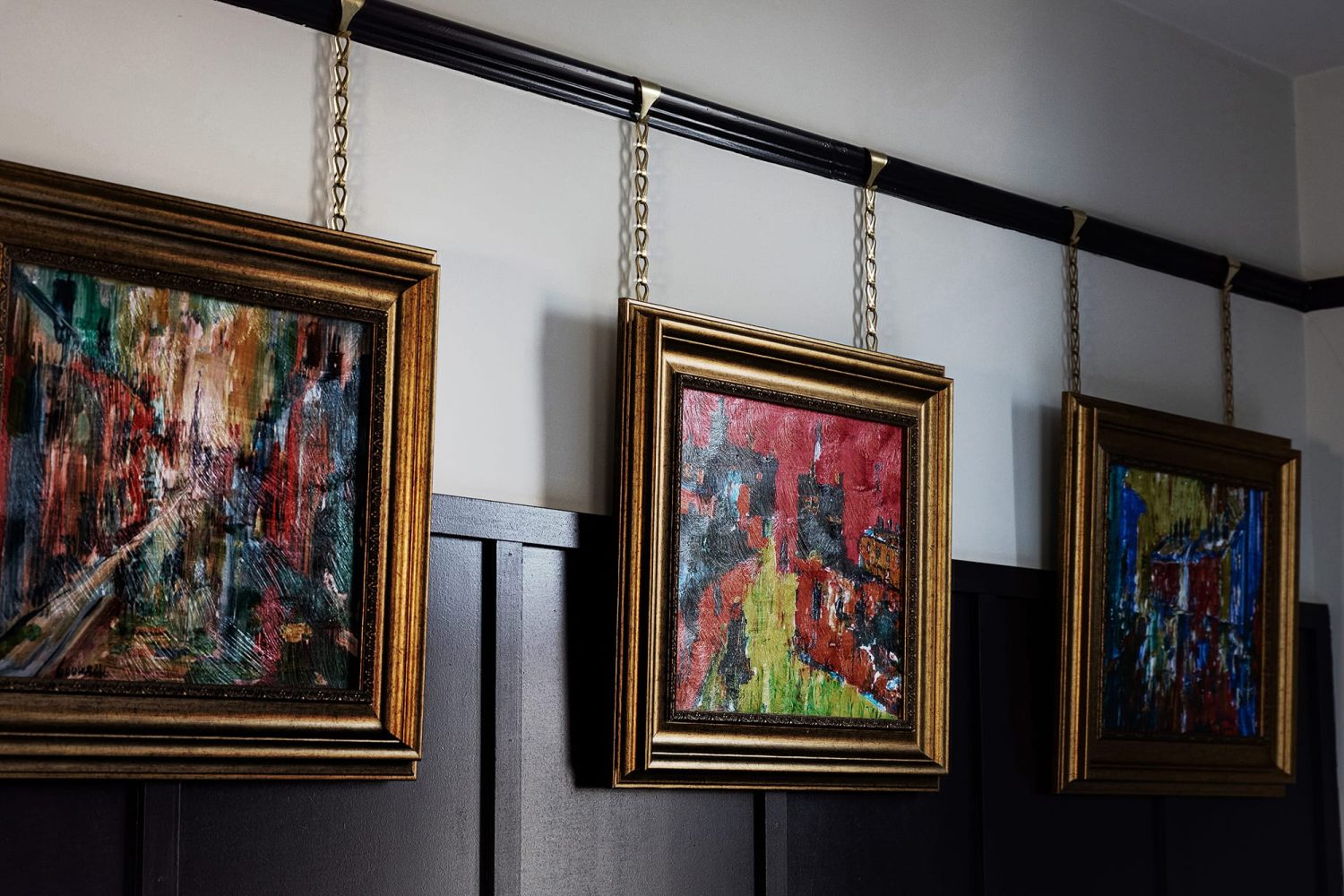 Gold frame painted artwork hung from gold chains along wall