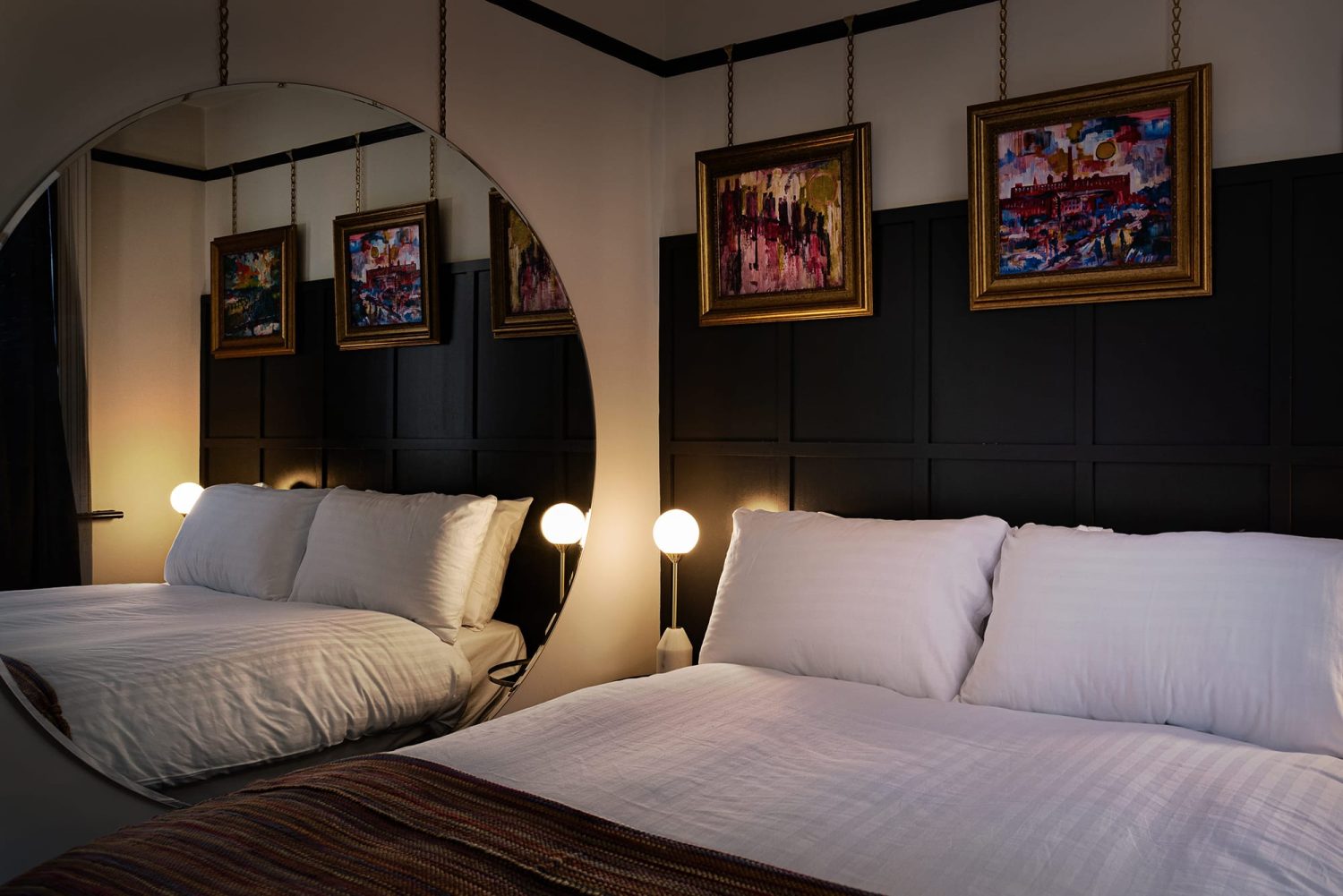 Bedroom with dark panelled walls behind double bed with large circular mirror on wall beside and gold framed artwork hanging above bed