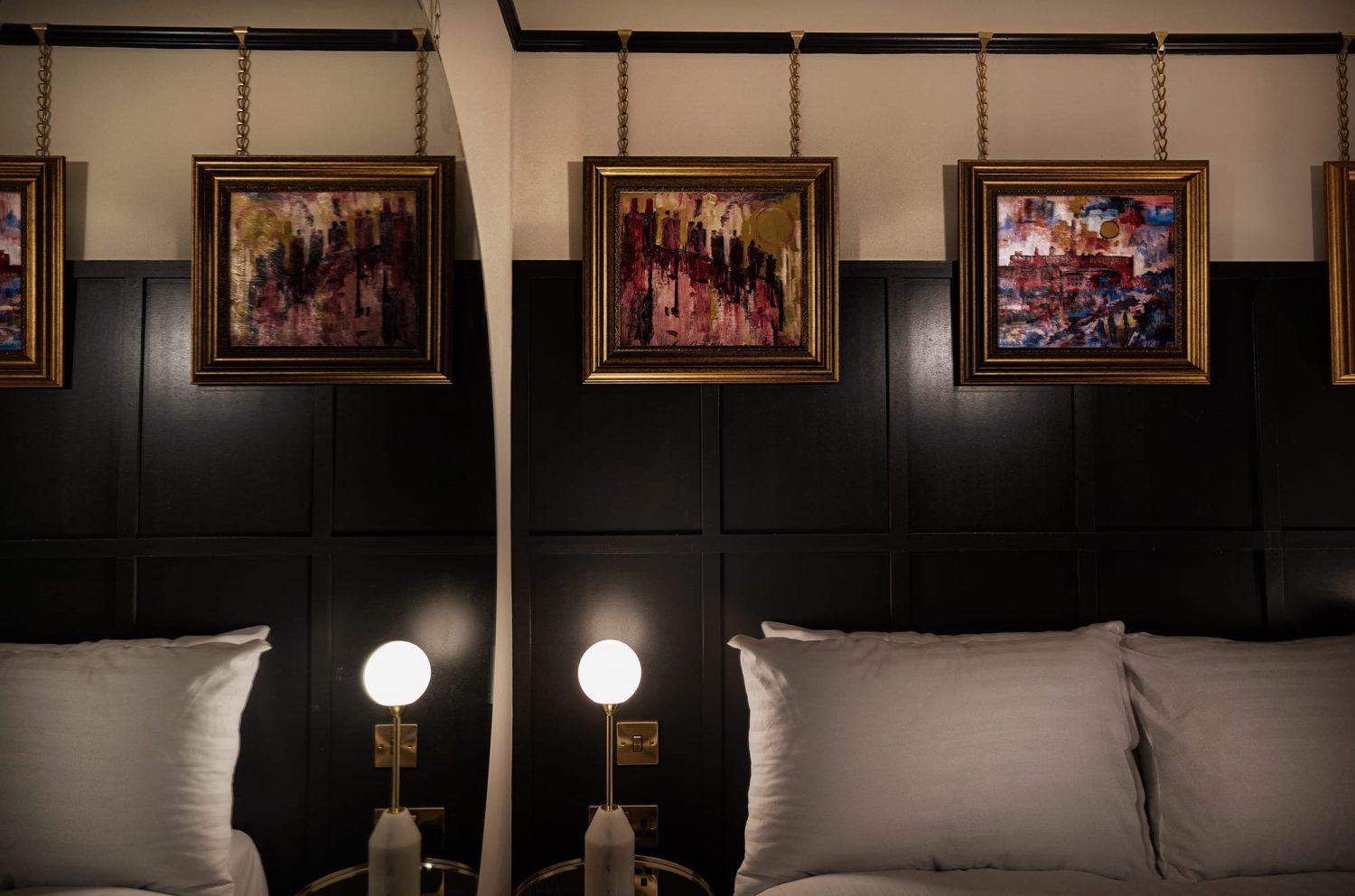 Corner of bedroom with large circular mirror on wall and dark painted panels on other side with gold framed artwork hanging above bed