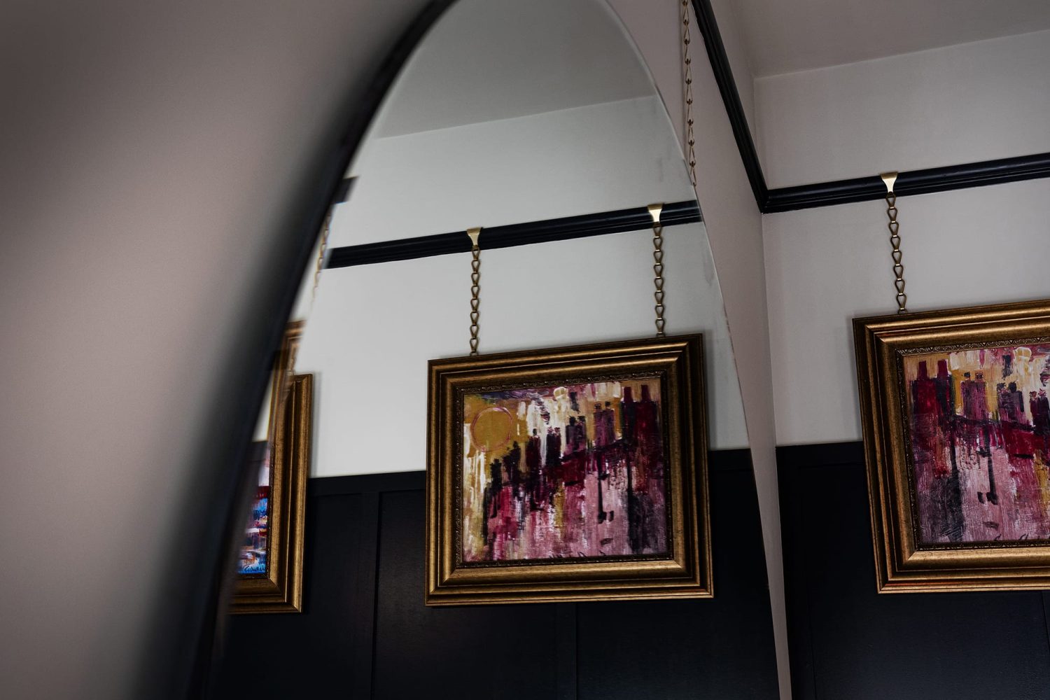 Gold framed artwork hanging on wall in reflection of a large circular mirror on the wall
