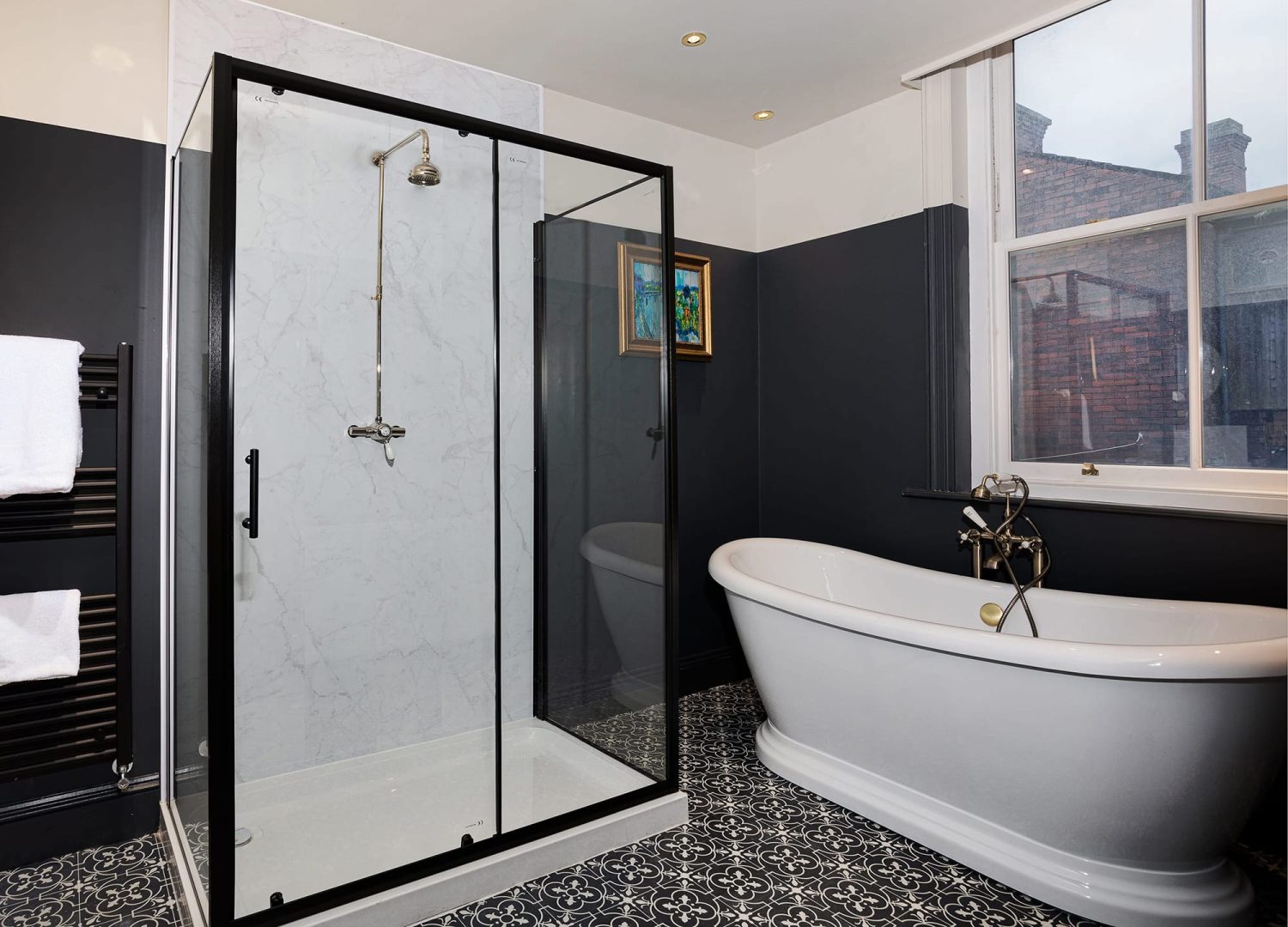 Shower with black framed glass surrounding next to large white bath and dark painted walls surrounding