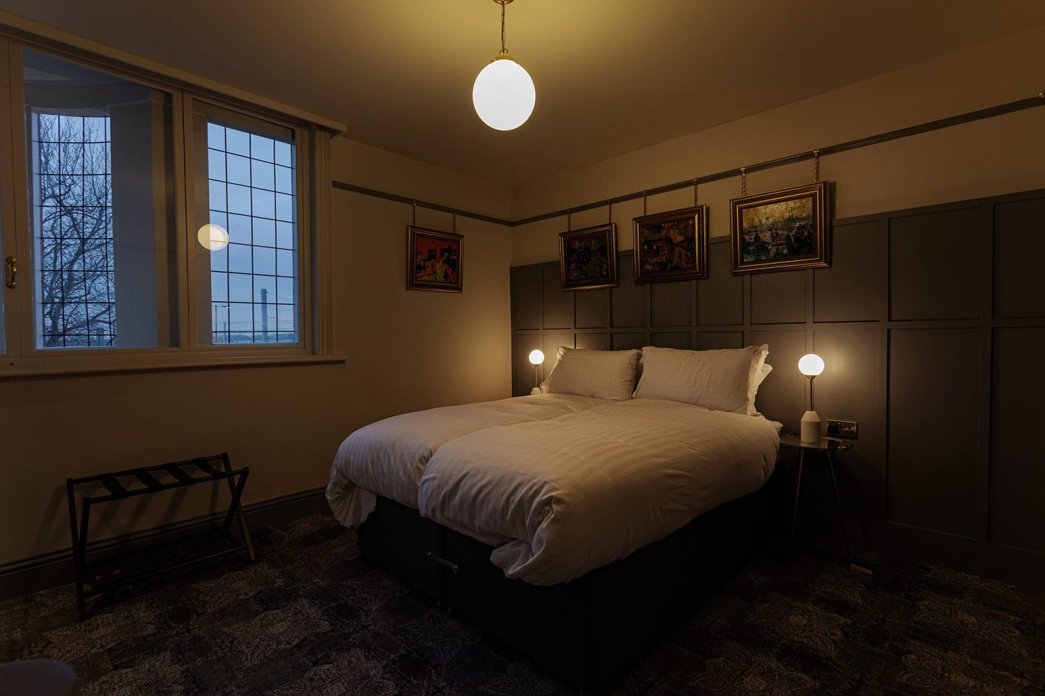 Bedroom with double bed against dark panelled wall with artwork hanging above bed and sphere pendant light hanging from ceiling
