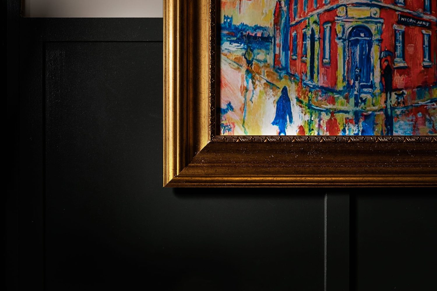 Corner of a gold framed painting on a dark panelled wall