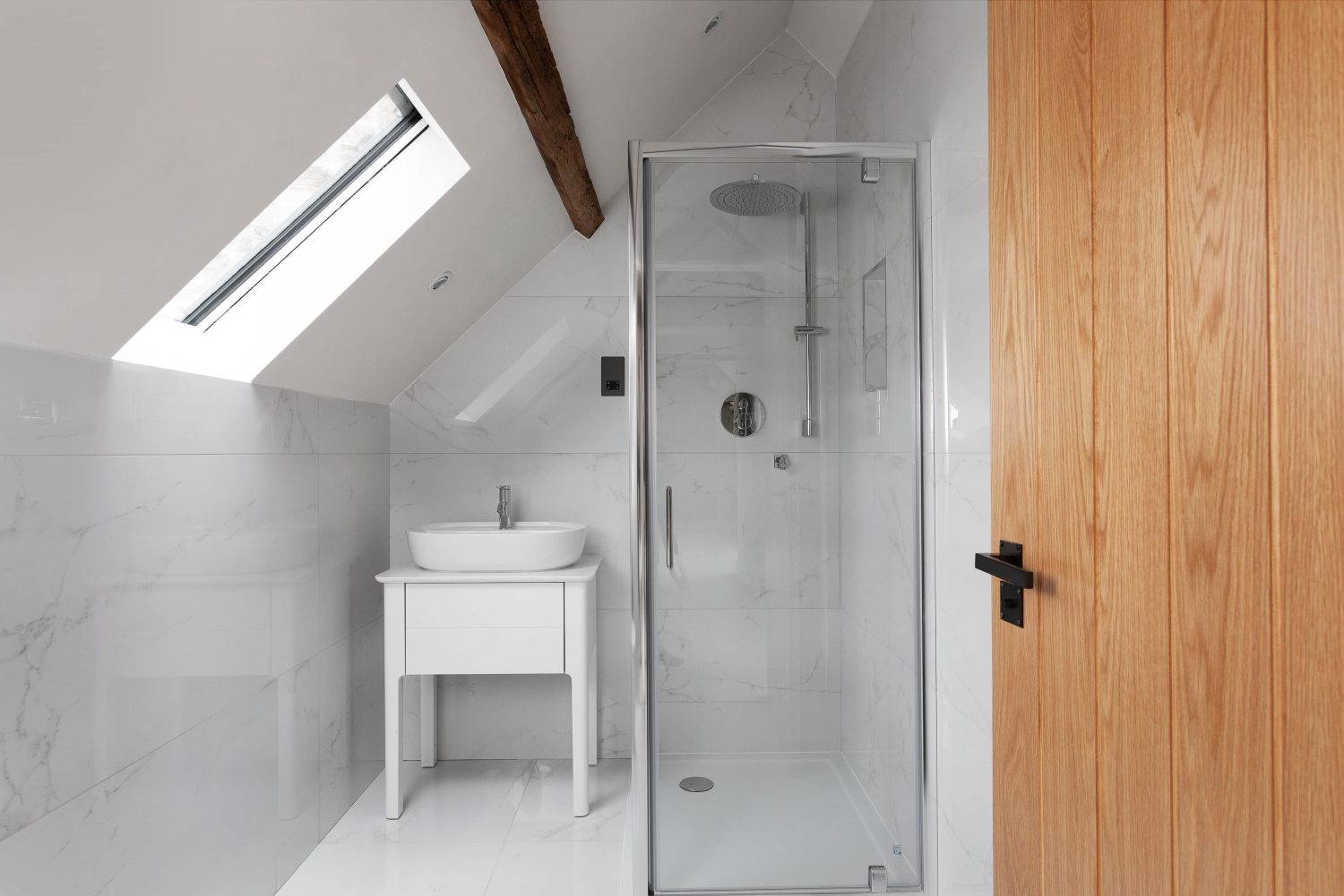 Bathroom with white marble walls and silver shower unit beside white sink unit with slanted ceiling above