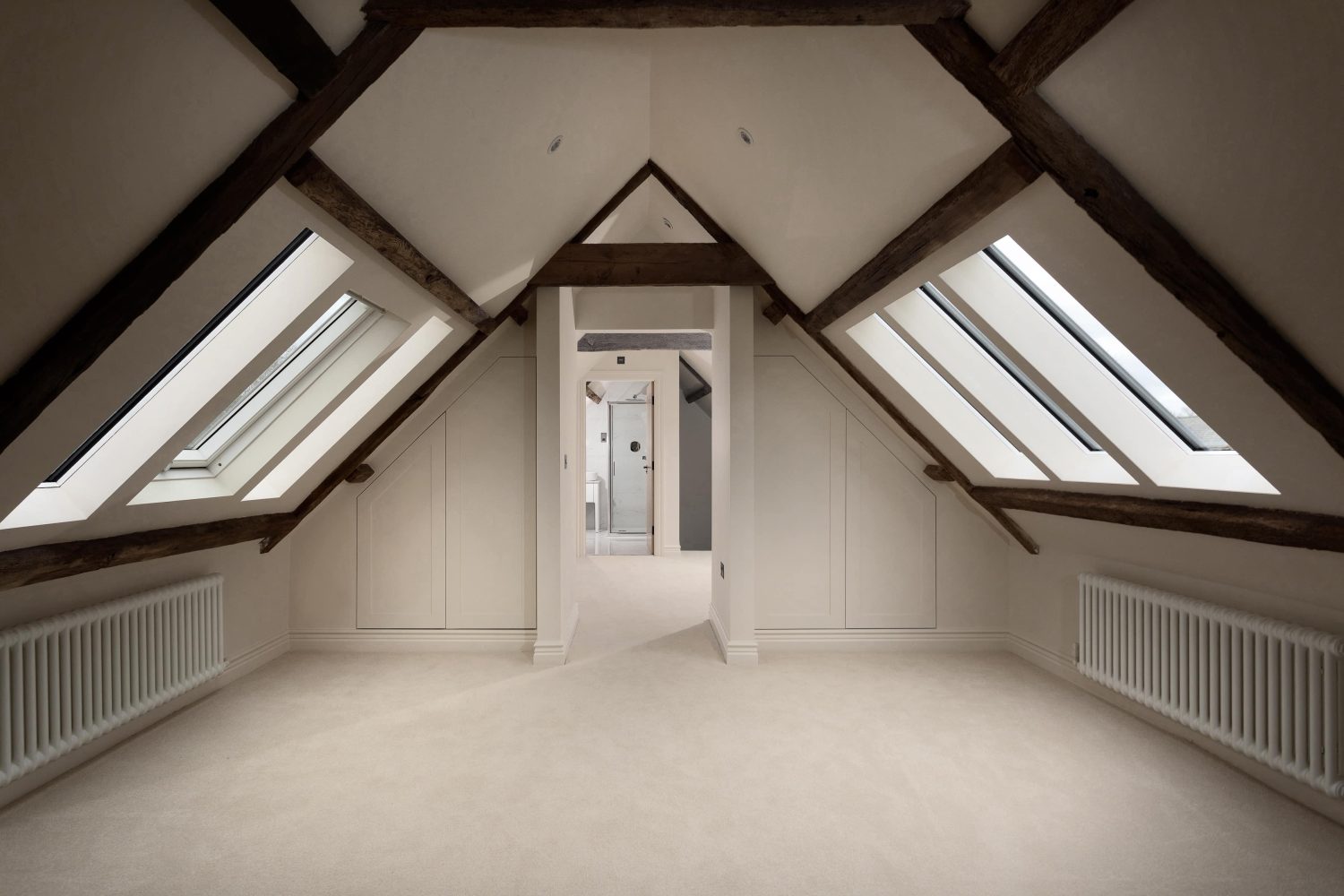 Loft room with slanted ceilings and windows on each side with doorway through to other room in the centre