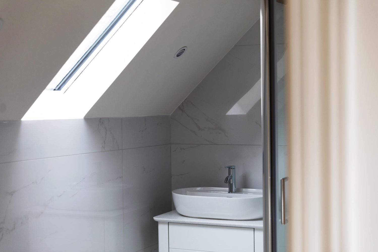 White bathroom sink with chrome tap and window on slanted ceiling above