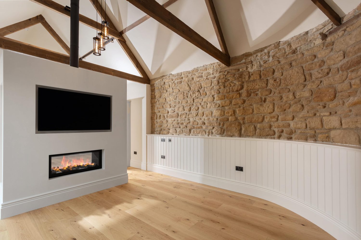 Media wall with TV and fireplace beside exposed stone curved wall with wooden beams above