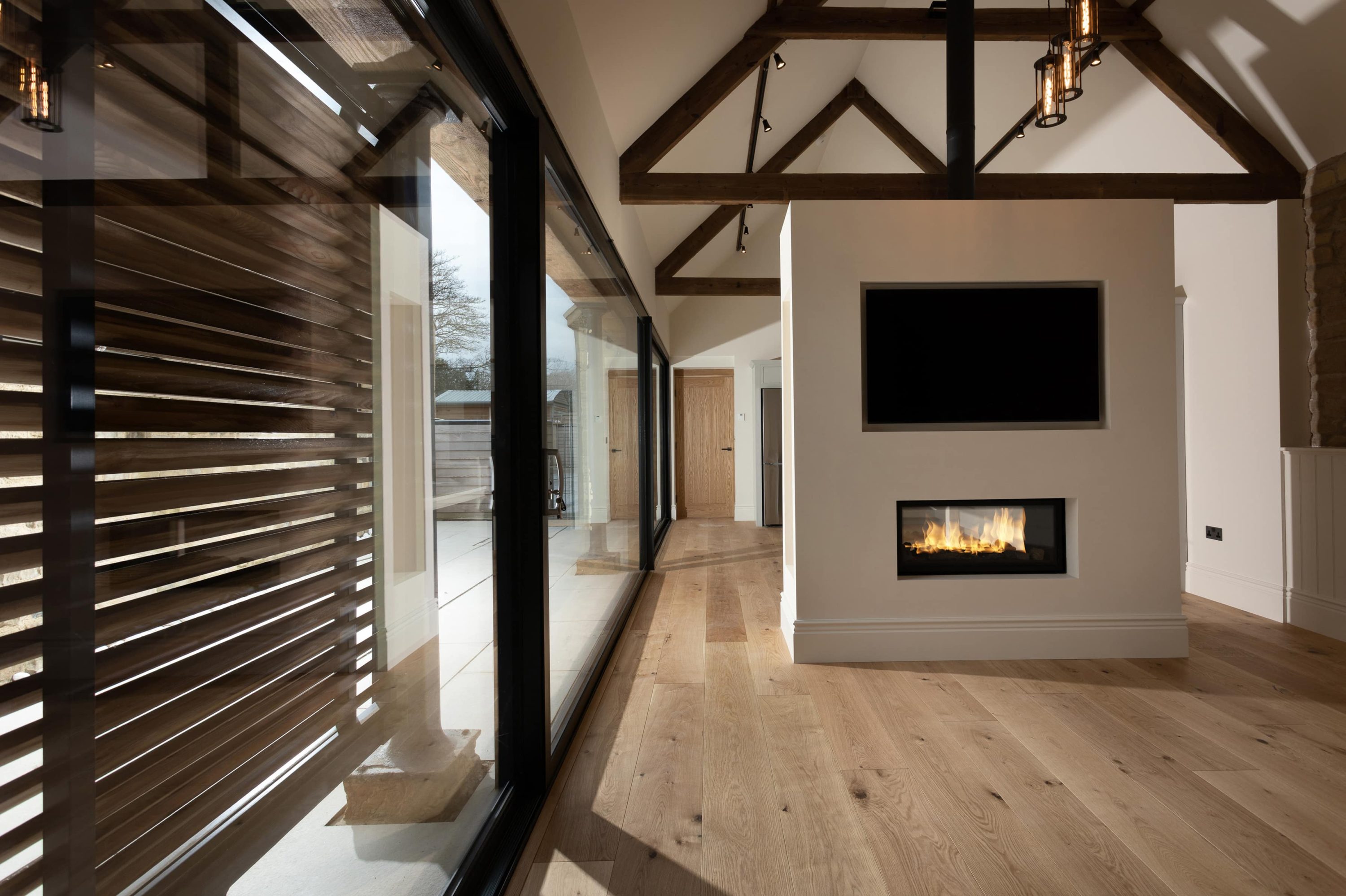 Media wall with TV above fire next to large glass sliding doors with black frames and wooden shutters