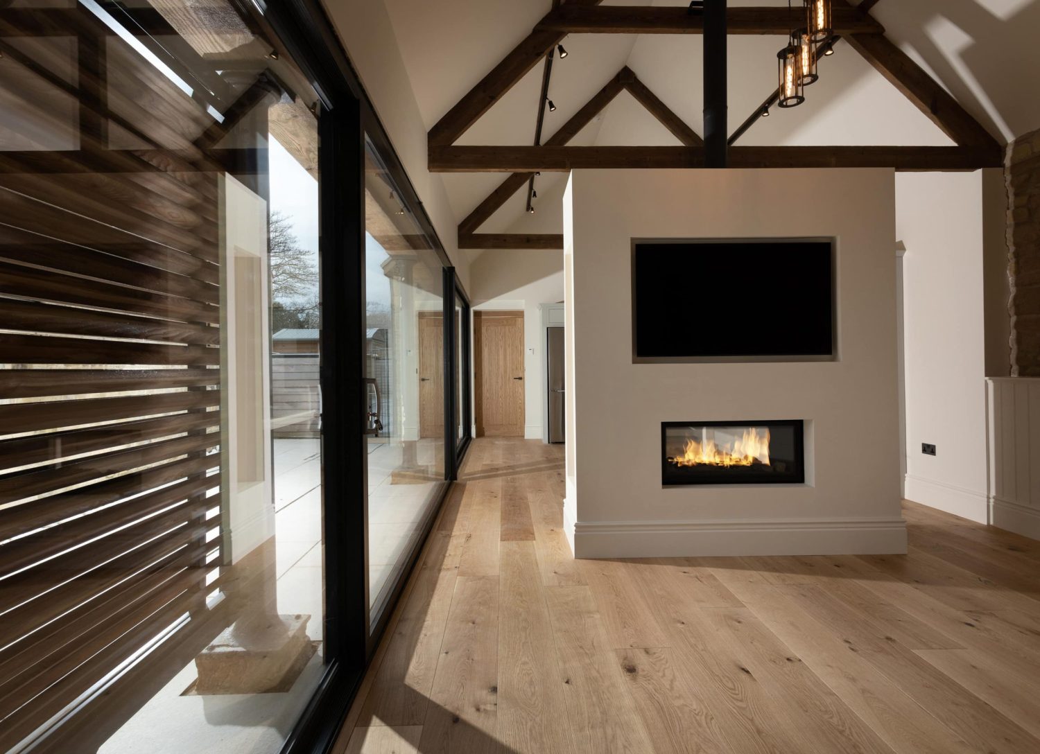 Media wall with TV above fire next to large glass sliding doors with black frames and wooden shutters