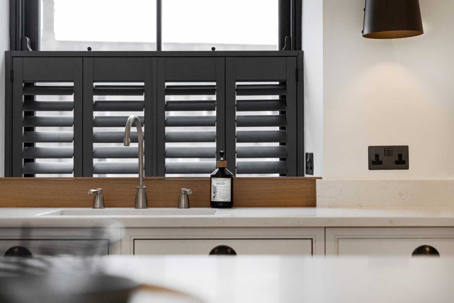 Silver kitchen sink with white counter top and window behind with dark grey shutters