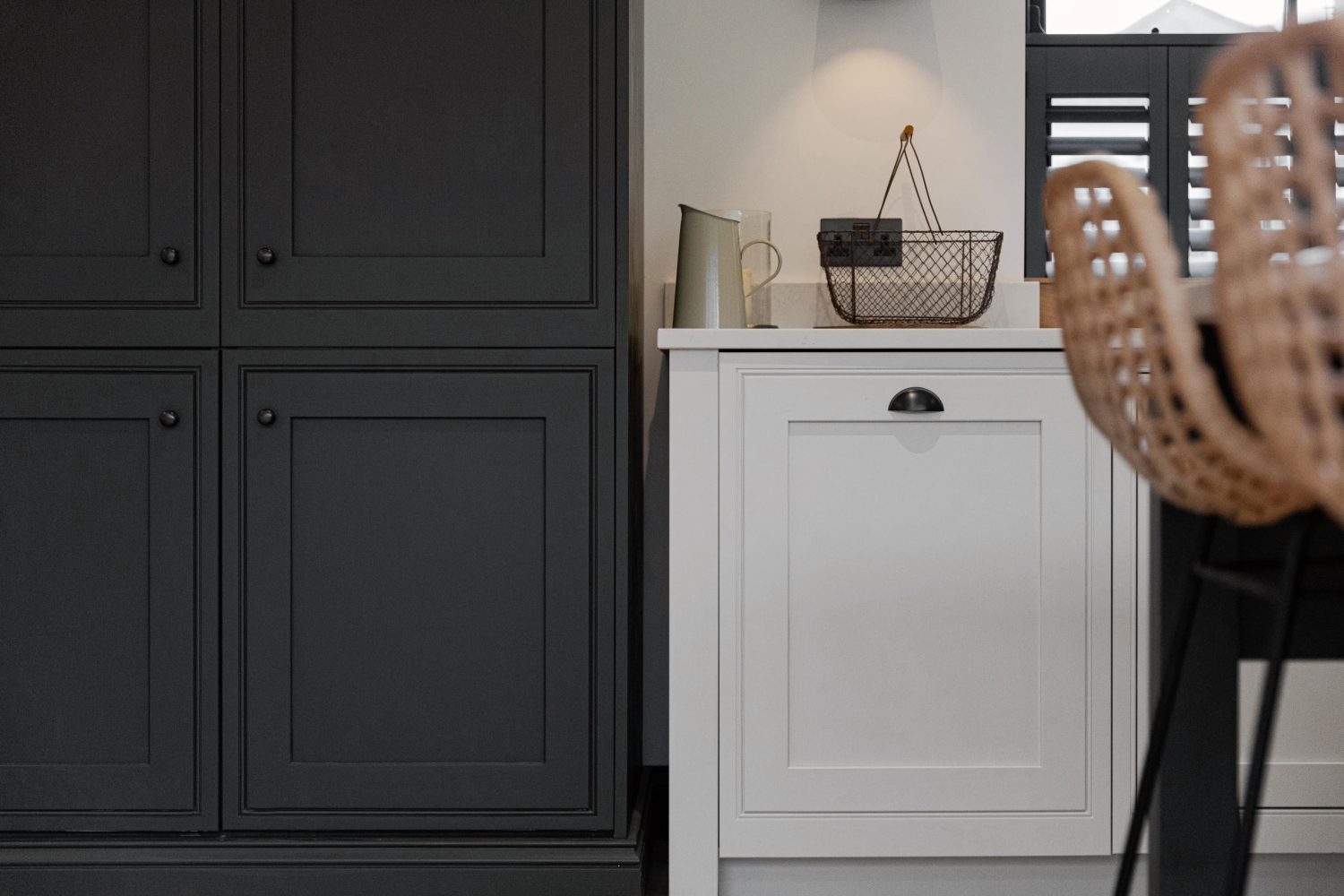 Dark grey double door cupboard beside white kitchen cabinets with barstools to the side