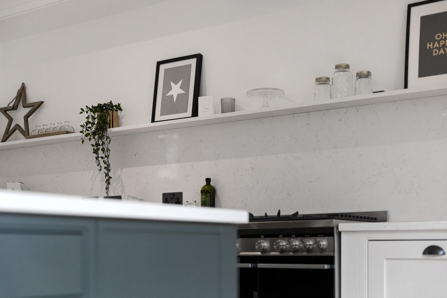 Long shelf above kitchen stove with white marble back splash with plants and framed artwork on top
