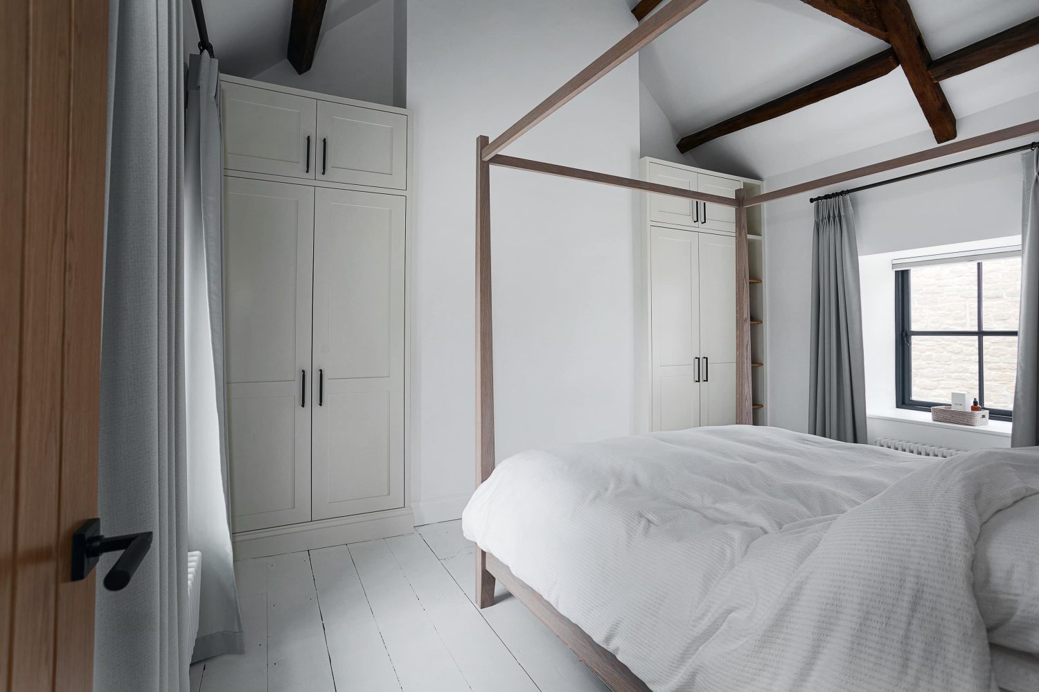 Wooden four poster bed with white wardrobes and wooden beam ceiling above