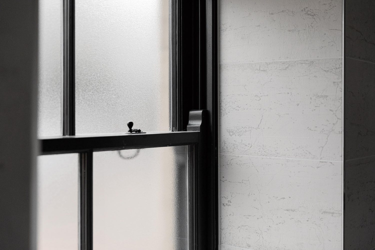 Black framed window with frosted glass beside grey marble wall