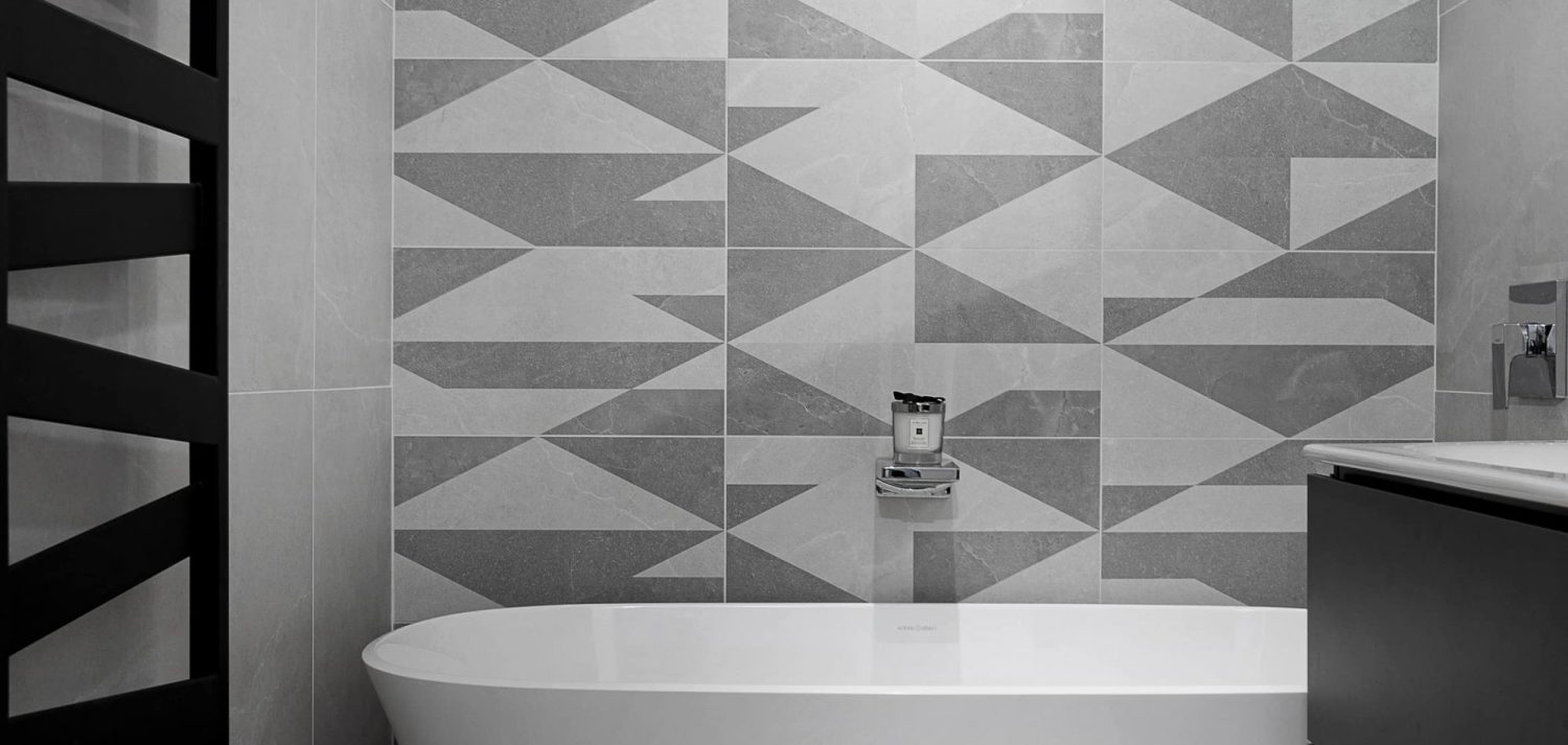 Large white bath with grey geometric pattern wall behind and chrome details