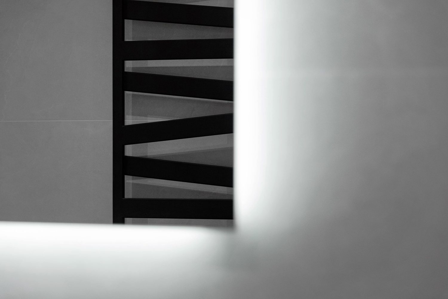 Black radiator with slanted rails in bathroom mirror against grey wall