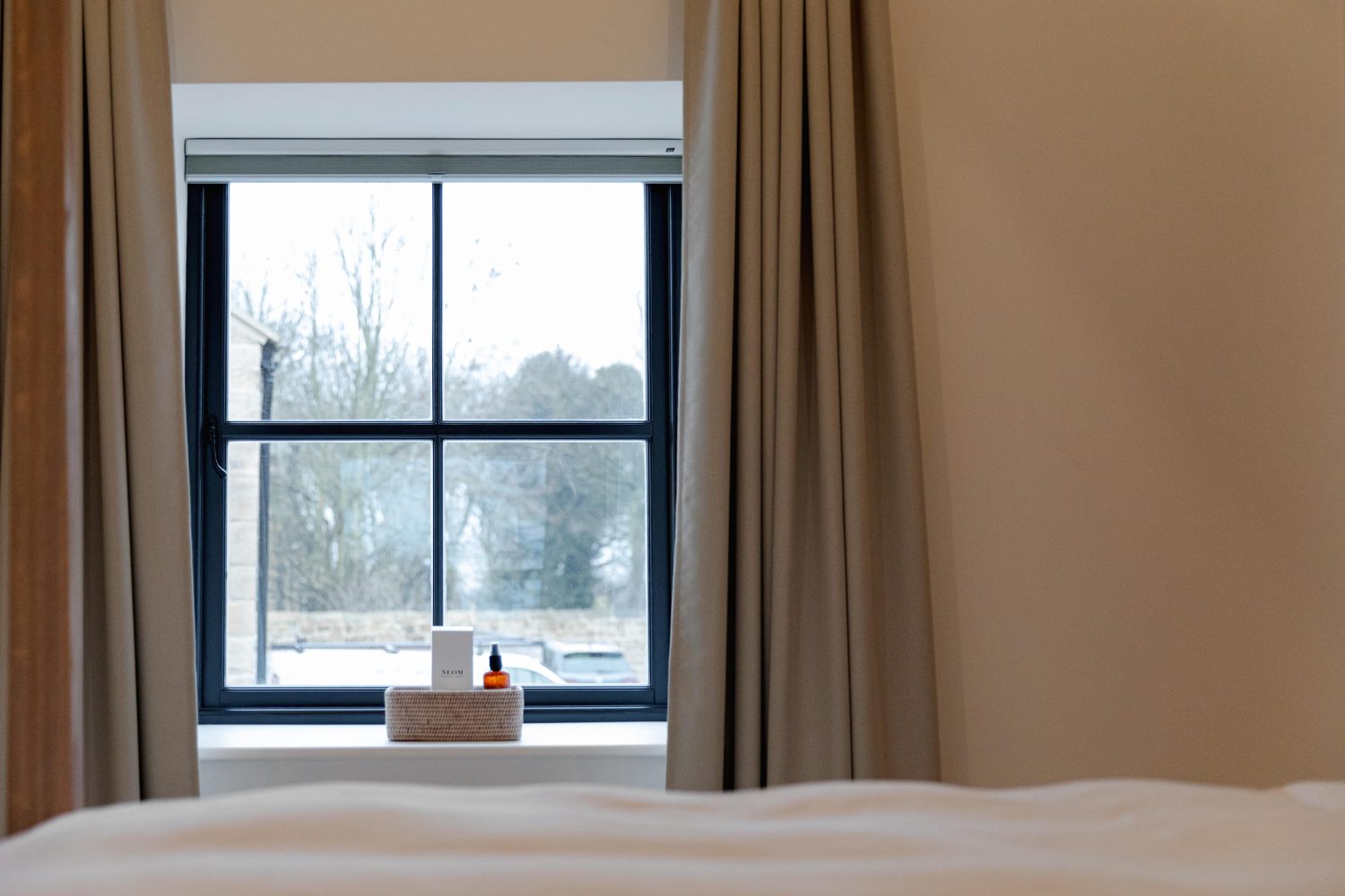 Black framed window in bedroom with long grey curtains and wicker basket on windowsill