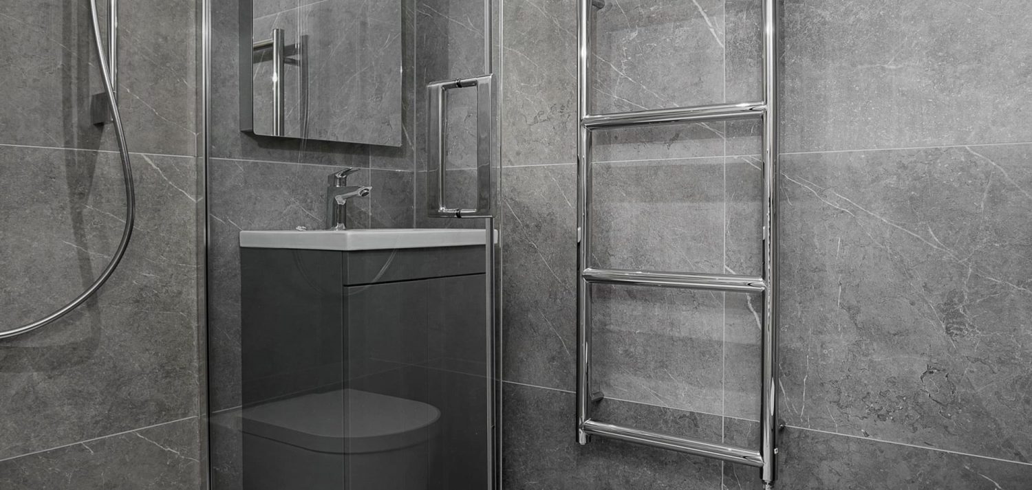Grey marble bathroom with chrome towel rack radiator and dark grey sink unit with chrome tap