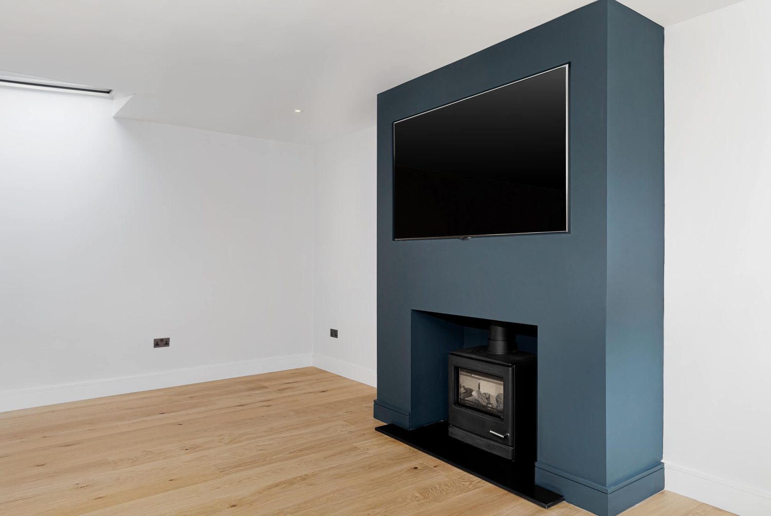 Room with white walls and muted blue media wall with large TV above black log burner
