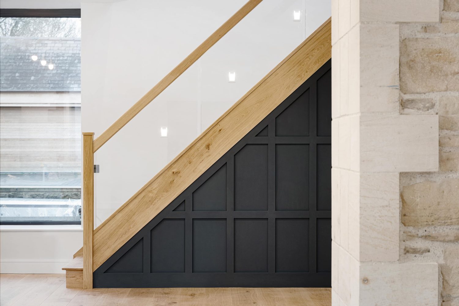 Dark blue panelled staircase with wooden banister and exposed stone wall in front