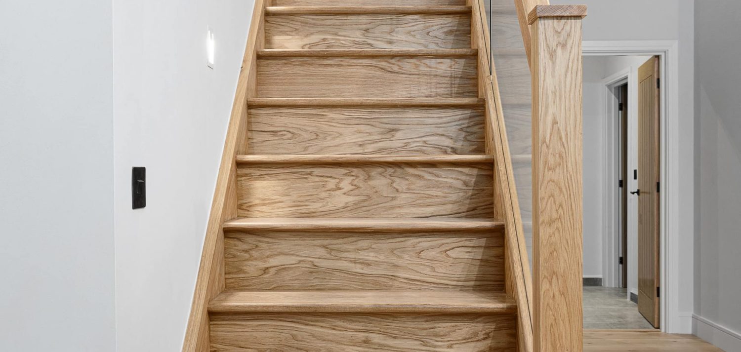 Close up on wooden staircase with white wall and glass barrier at the sides