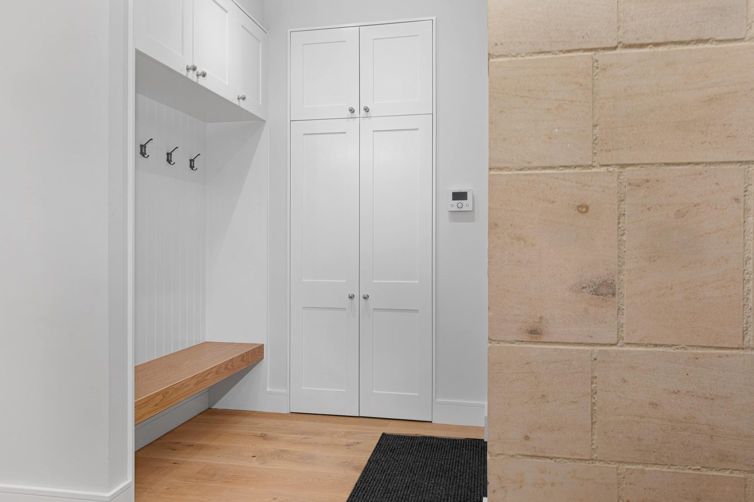 White coat rack area with double door cupboard and exposed stone wall