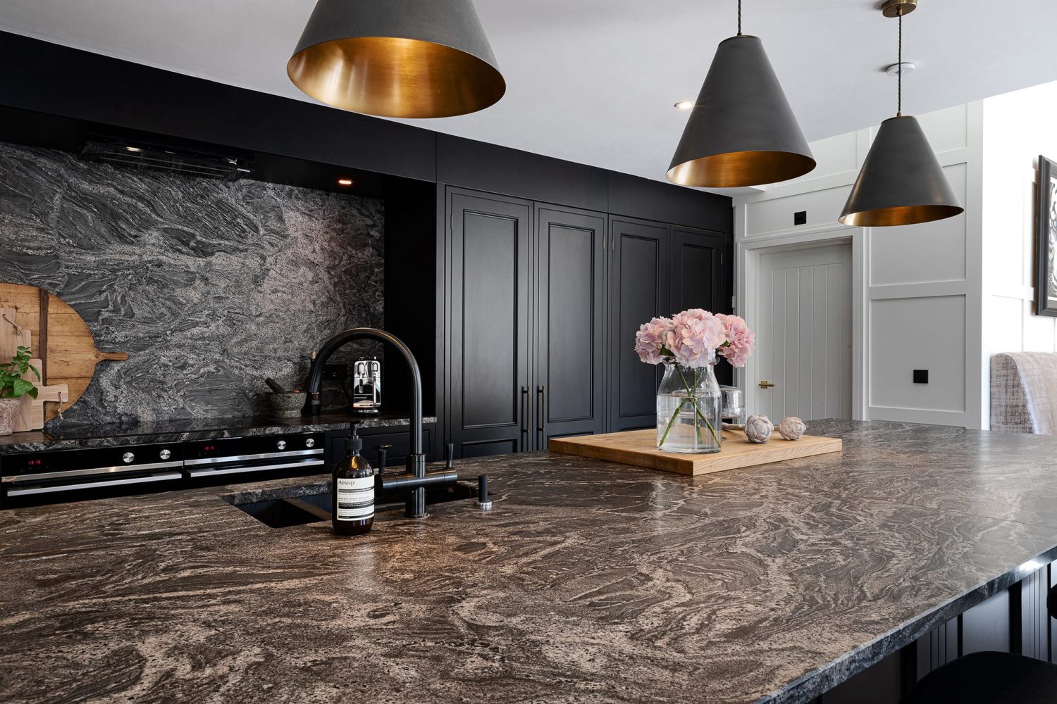 Large kitchen island with dark grey marble countertop and black sink with black cabinets behind