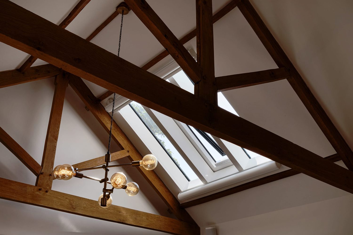 White ceiling with wooden beams across and large pendant light hanging down in the centre