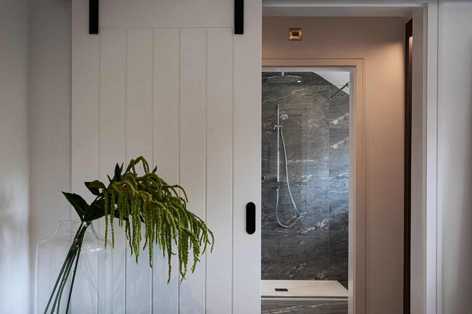 White panelled sliding door opening up to shower in bathroom with dark marble walls